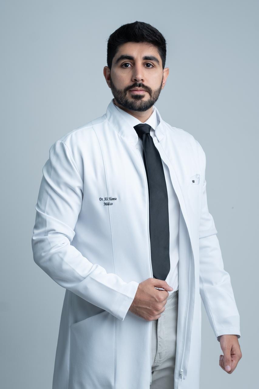 Dr. Ali Hamie de jaleco branco, com o nome e a palavra Médico bordados no peito.
